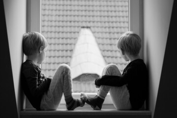 dwóch chłopców bliźniaków siedzących przy oknie - obrazy, fototapety, plakaty