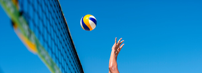 Athletic man jumping to make wall block at beach volleyball net. Horizontal sport poster, greeting...
