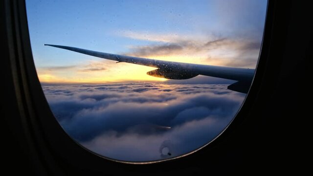View through dirty fogged airplane window onto wing at sunset. plane flies into clouds at dusk or dawn and prepares for landing, cinematic view of clouds with golden sun.