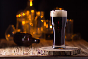 A glass filled with beer on a wooden table on a dark background with yellow bokeh lights.