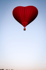 A hot air balloon flies over a green field. Composition of nature on a background of blue sky.