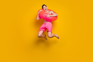 Fototapeta na wymiar Full length photo of young man happy positive smile jump up circle float buoy trip isolated over yellow color background