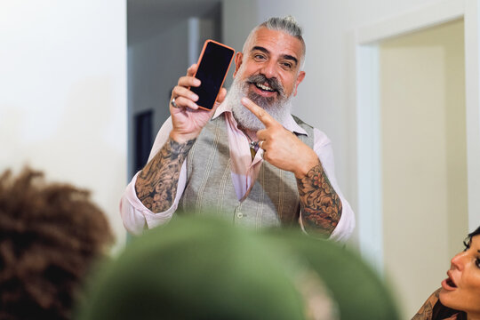 Adult Hipster Man Pointing Finger On Smartphone Screen - 50s Guy Showing Cellphone Device During A Home Party To His Friends.