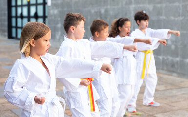 Fototapeta na wymiar Group of concentrated preteen children learning karate movements during outdoors class in schoolyard on summer day