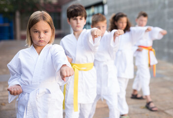Fototapeta na wymiar Kids in kimono doing kata moves on street during outdoor karate training.