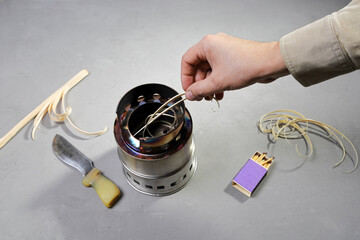 Hand folding wooden shavings in compact burner for firewood to ignition fire for heat, on gray...