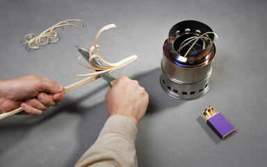 Hands cuting knife shavings for firewood compact burner to ignition fire outdoors on gray concrete...