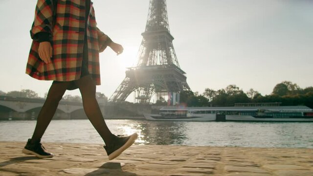 Unrecognizable Woman in dress and sneakers Walks in Paris, France, with Eiffel Tower at background. Stylish Female Tourist Traveling to Main European Landmark on sunny day. 4K tracking medium shot