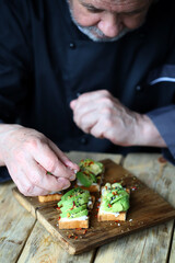 Chef prepares avocado toasts on a wooden board.