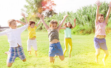 Positive kids jumping and raising hands up on green field.