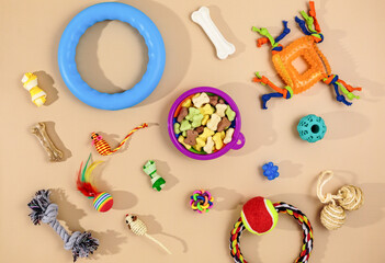Different multicolored pet care accessories: bowl, bones, balls, snacks, mouse on beige background. Rubber and textile accessories for dogs and cats. Top view, flat lay.	