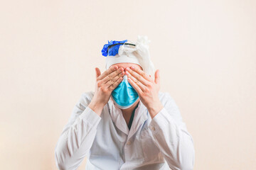 Shocked doctor with hands on his eyes in protective medical mask and white lab coat isolated