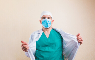 Doctor in protective medical mask and green suit opens his white coat isolated