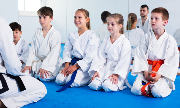 Young positive man training new moves with children during karate class