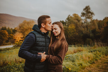 Young man and woman in autumn clothes hugging and kissing against autumn mountain forest. Copy space.