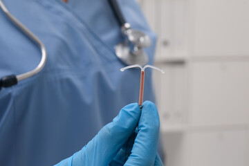 Doctor holding T-shaped intrauterine birth control device on blurred background, closeup