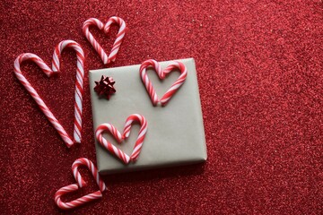Christmas background. Wrapped present with red bow and five candy cane hearts on red glitter background.