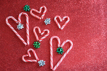 Christmas background. Six candy cane hearts and green and silver bows on red glitter background.