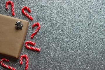 Christmas background. Wrapped present with silver bow surrounded by red and white candy canes on silver glitter background.