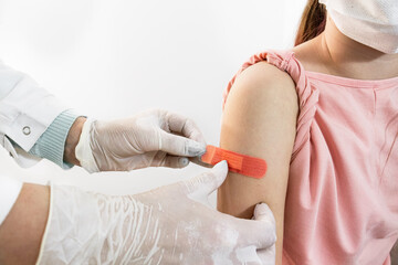 The nurse's hands are wearing rubber gloves and applying a medical tape to the injection site on the shoulder of a child sitting next to him. Close up. Selective focus. 
