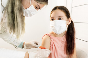 A nurse in rubber gloves and a protective mask glues a medical plaster to the injection site on the shoulder of a child sitting nearby in a mask. vaccination of children and injections.  
