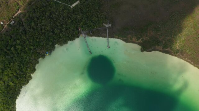 Aerial birds eye overhead top down view of colourful lake surrounded by forest. Shadow of moving clouds going through footage. Kaan Luum lagoon, Tulum, Yucatan, Mexico