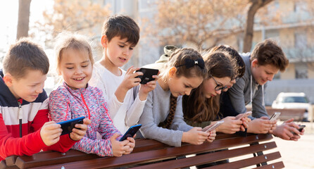 Group of children playing with smartphones outdoors at sunny spring day - obrazy, fototapety, plakaty