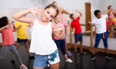 Fototapeta na wymiar Portrait of little girl doing exercises during group class in dance center
