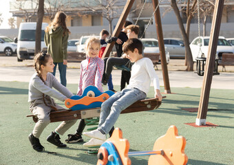 Kids spending time together outdoors playing and talking on see-saw and spring rider