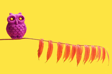 An purple owl glitter toy bird with yellow eyes sitting alone on a colorful leaves tree branch....