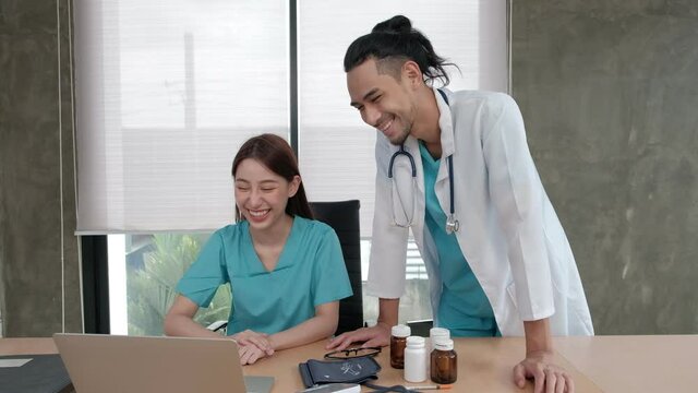 Healthcare team partners. Two uniformed young Asian ethnicity doctors are coworkers discussing medication in hospital's clinic office. Specialist persons are experts and professionals.