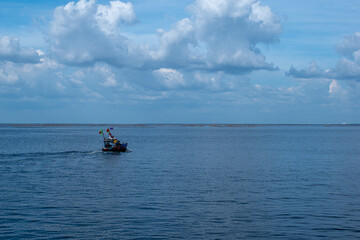 Obraz premium A small boat floated in the sea, the sky was blue with white clouds.