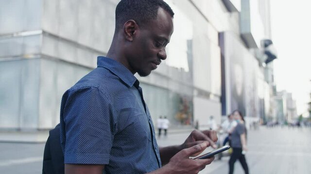 Side view of Young African man using mobile phone sending message in the urban city street of Chengdu China at afternoon