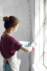 Woman in a white apron paints a window in a house interior renovation
