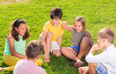 Fototapeta premium Young boys and girls sitting on green grass and discussing something funny.
