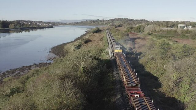 Following aerial of freight train hauling railroad tracks along river