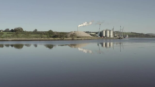 Riverside cement plant in Ireland with tall smoke stack seen beyond
