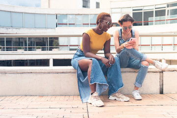 a couple of young stylish women smiling and watching smartphone outdoor. High quality photo