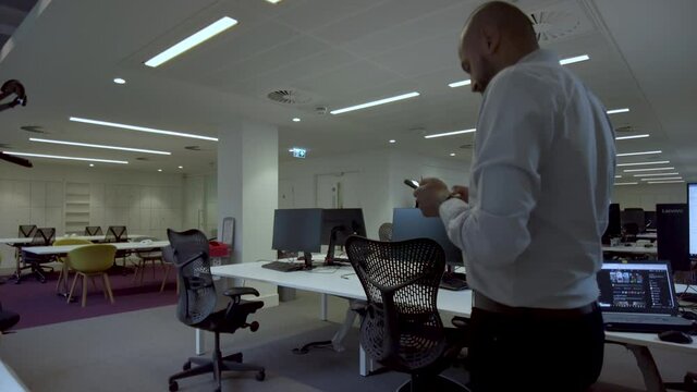 A well dress Indian business executive anxiously pacing up and down an empty office, drafting an important text message on his mobile phone after business hours