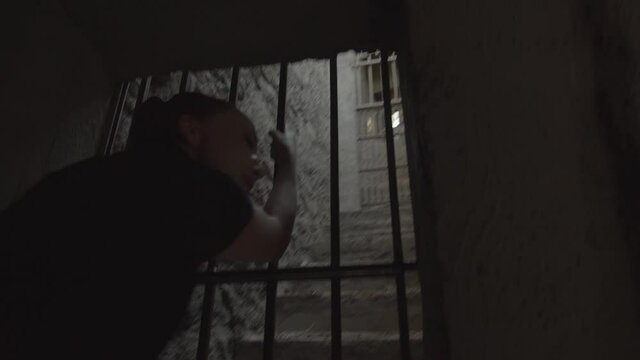 Artsy conceptual footage of a woman reaching up through old prison bars up a stairway