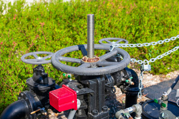 Manual hand wheel on valve controlling the main water supply system. Blurred green landscape background.