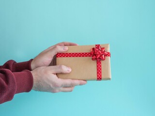 Male hands are holding a gift box with a red bow and satin ribbon on a blue background.