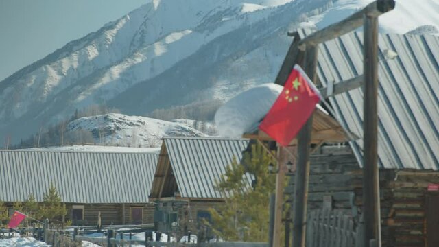 Snow covered rustic wood cabins with Chinese flag hanging outside
