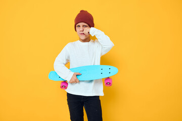 Cheerful little kid in a red hat skateboard in his hands yellow color background