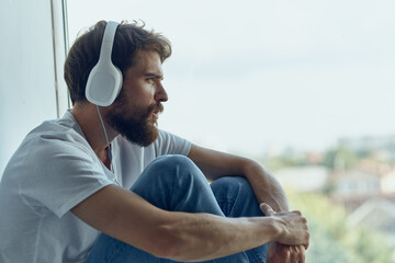 bearded man sitting near the window in headphones listening to music