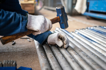 Action of a worker is using iron stamp plate to mark serial number on metal pipe specimen. Industrial action and equipment photo. Selective focus on the object in hand.