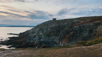 Aerial of ocean scenery with young attractive woman taking photo of Mountain cliffs at the Seaside during sunset. Traveler Tourist Woman sitting on blanket taking photos of nature and house.