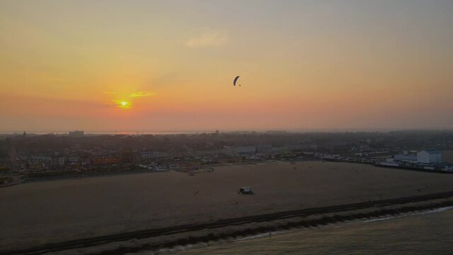 Great Yarmouth beach resort, Norfolk. Pilot flies a motorised parachute or paraplane above the beach. Sun setting.