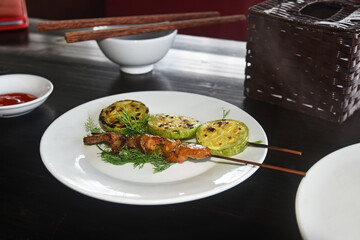 Grilled fish and zucchini slices on a white plate in a cafe on a wooden table