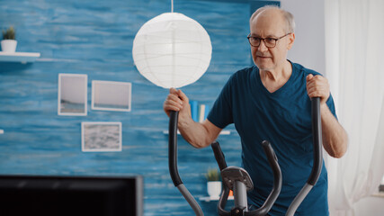 Close up of aged man doing cycle exercise on static bicycle at home. Senior person training with...